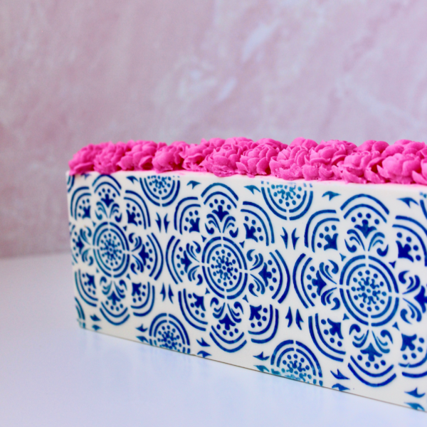 Side view of white soap with blue madallion texture with magenta piped soap flowers on top
