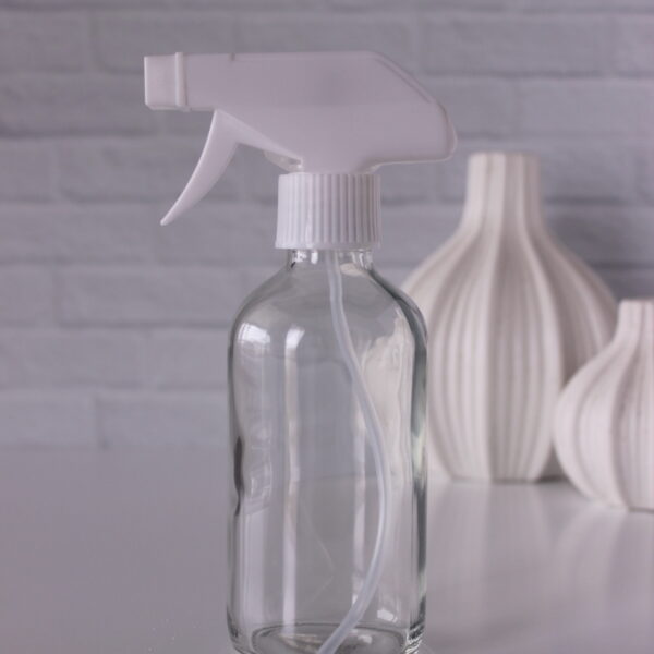 clear spray bottle in front of a white brick wall with two vases